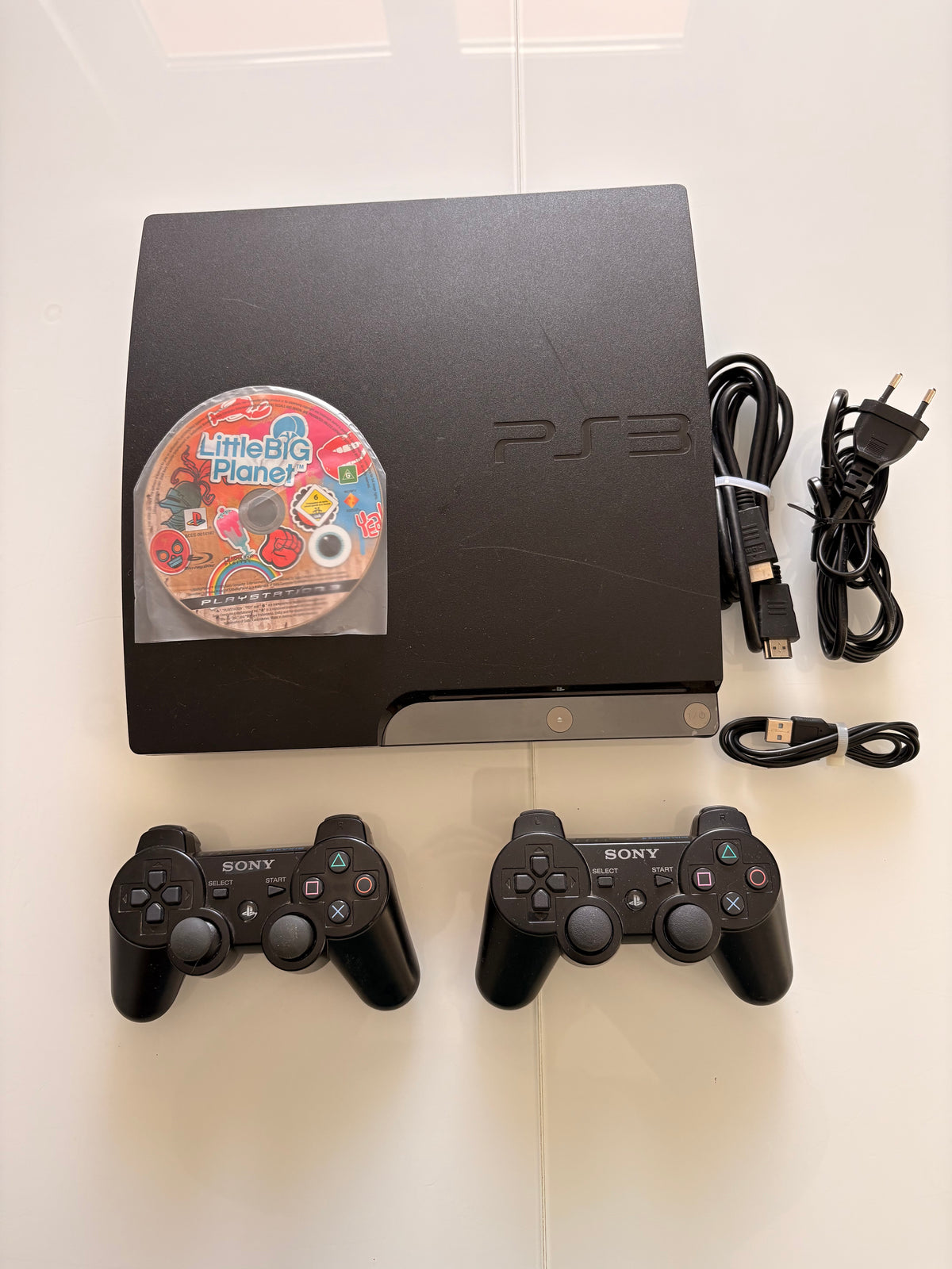 PlayStation 3 Slim (CECH-2004B) + 2 offizielle Sony-Controller + vollständige Verkabelung + Spiel LittleBigPlanet